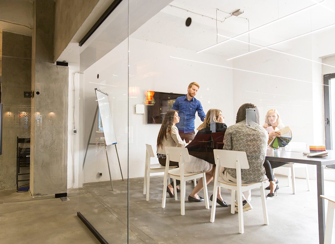 About Our Agency - Looking Through the Glass Windows at a Small Group of Employees Having a Meeting in a Modern and Bright Office