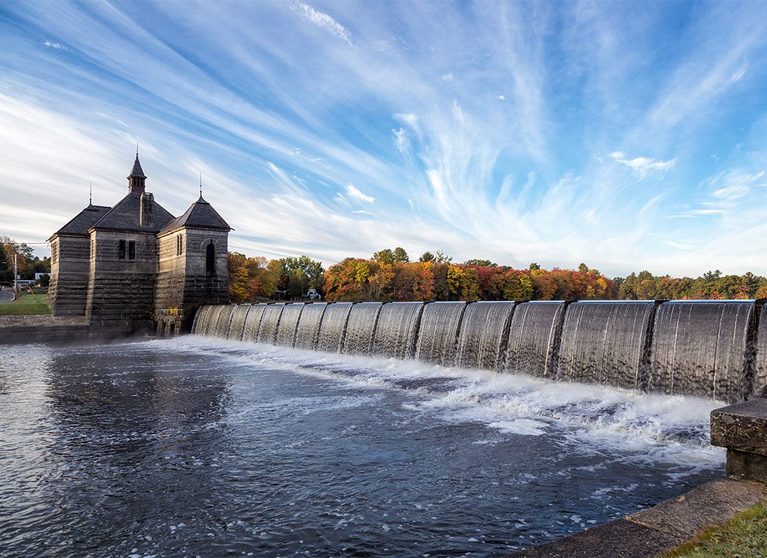 Framingham, MA - Water Flowing Through a Historical Dam in Framingham Massachusetts with a Cloudy Blue Sky and Colorful Trees in the Background