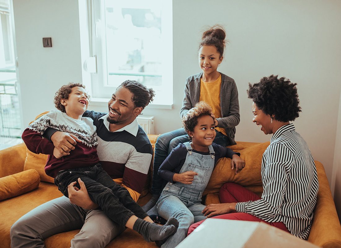 Personal Insurance - Portrait of a Cheerful Family with Three Kids Having Fun Spending Time Together While Sitting on an Orange Sofa in the Living Room