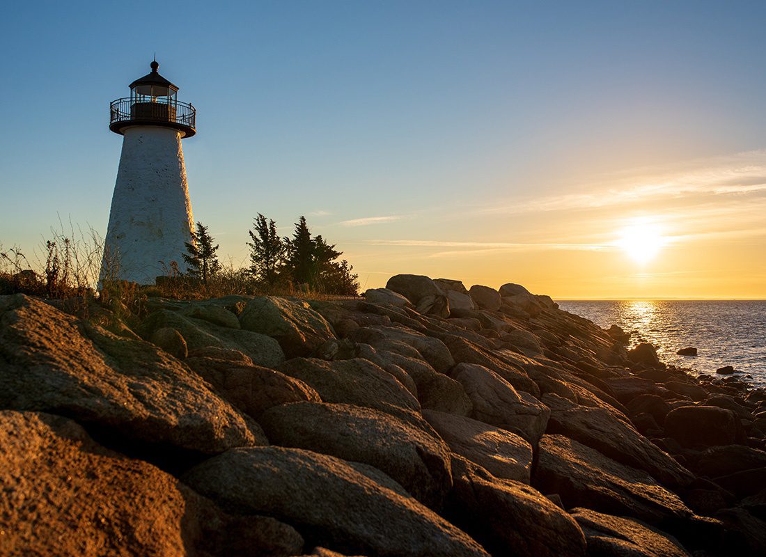 Plymouth, MA - View of a Lighthouse on a Rocky Edge Next to the Coast at Sunset in Plymouth Massachusetts