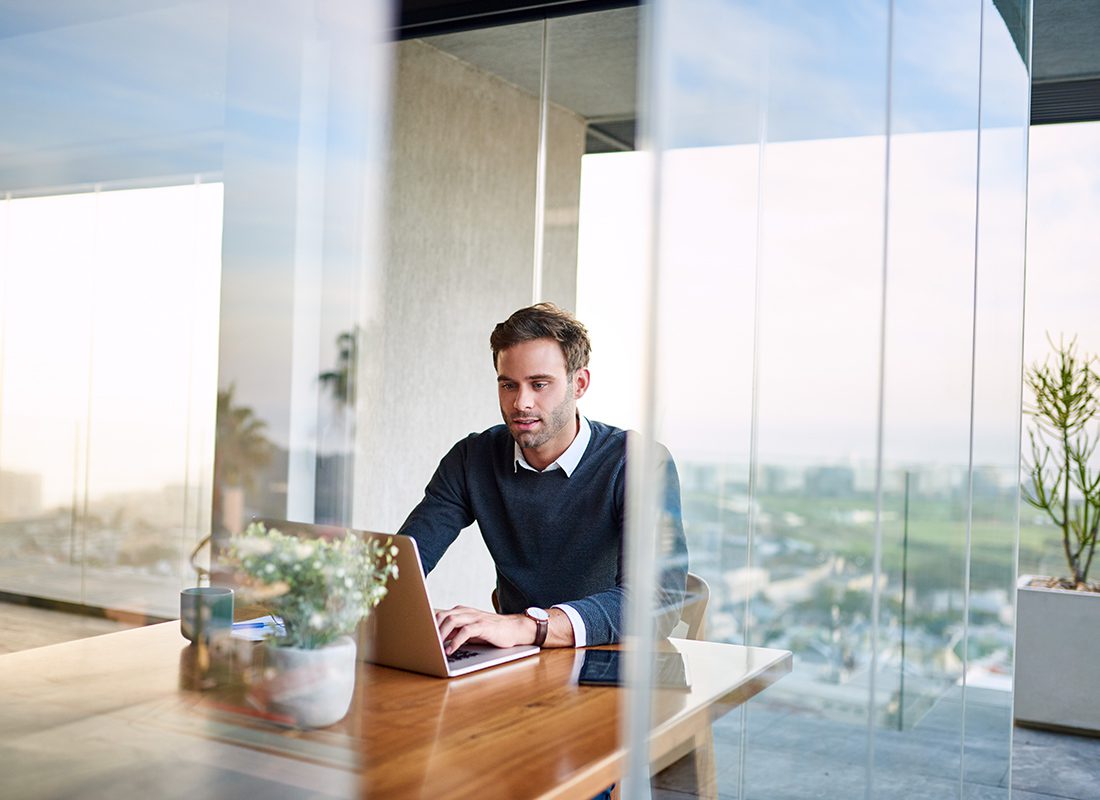 Blog - Professionally Dressed Man On Laptop Sitting at a Wooden Table in an Office on a Nice Day
