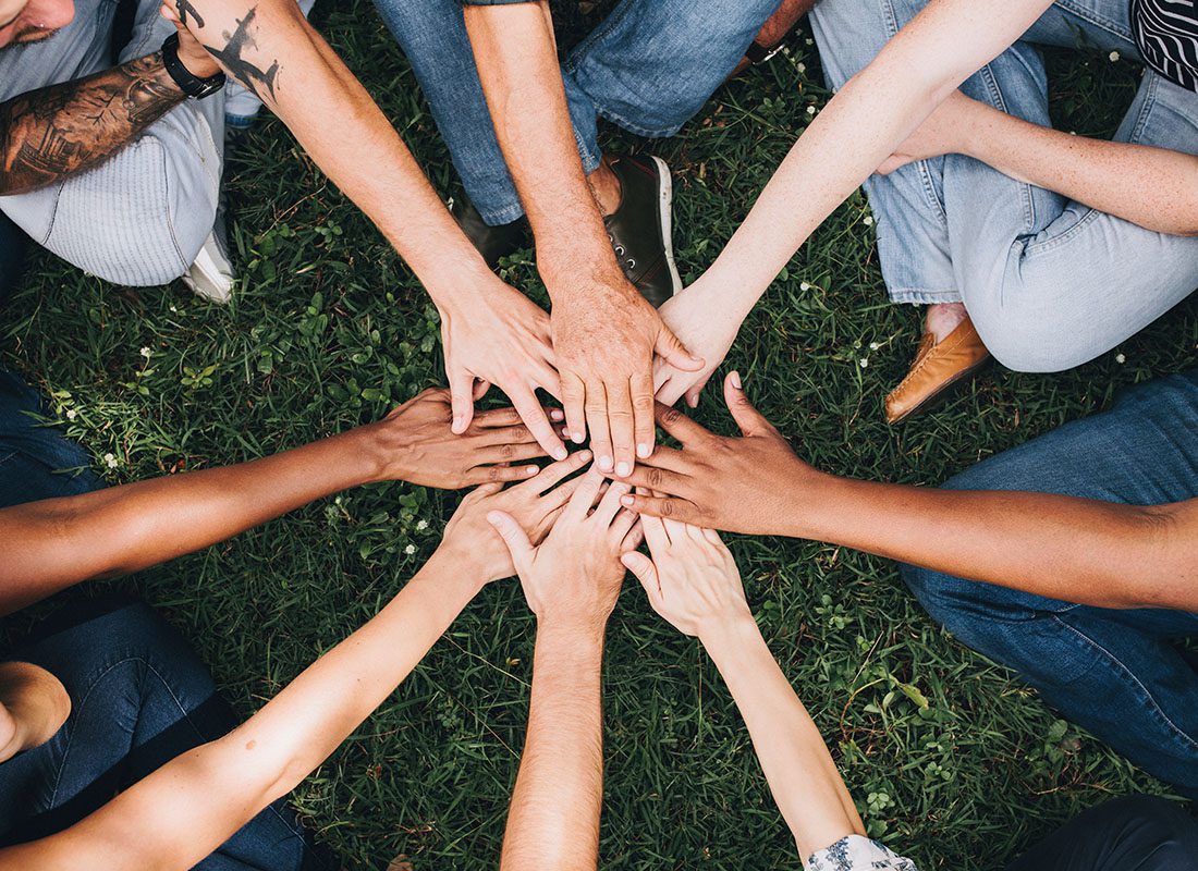 Charity Application - Close Up of People Putting Their Hands in the Center as They Stand in a Circle Outside in the Grass